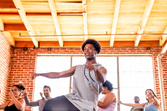 Diverse group in a dance class, led by a smiling man in a bright studio.