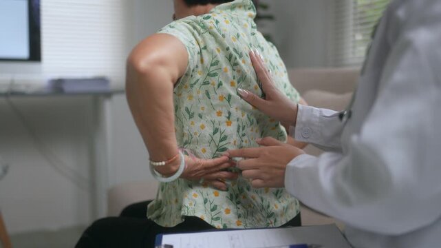 Female physician palpating the sore spine and lower back of an elderly patient during a medical examination in the clinic to diagnose the cause of her painful muscle injury or discomfort