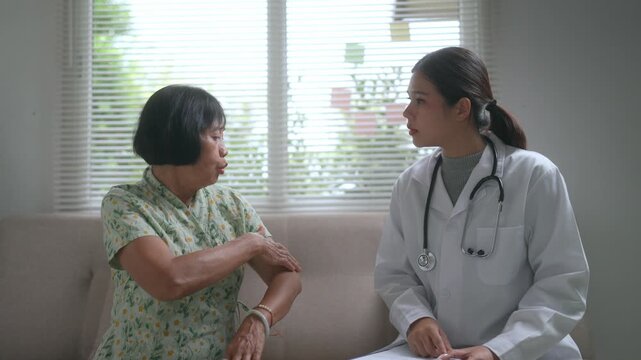 Senior asian woman describing shoulder pain symptoms to a caring female doctor during a home visit. Professional physician providing medical consultation and health checkup for an elderly patient