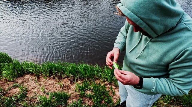 Fisherman rigging a soft plastic lure on a jig head for bass fishing on a riverbank