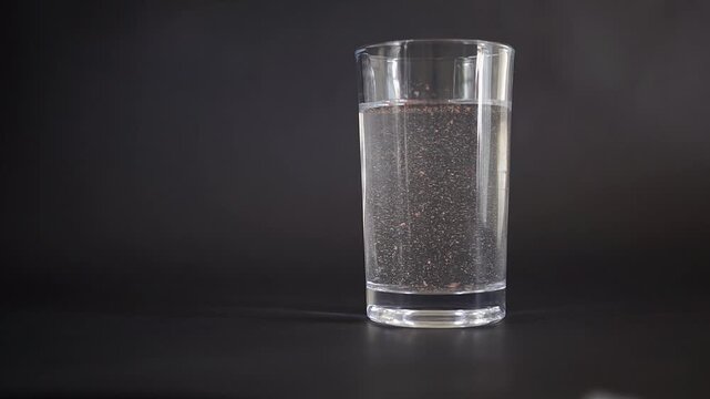 Glass of drinking water with floating microplastic particles inside on a black background, water contamination, plastic pollution, public health, and environmental concept