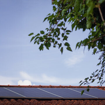 Residential Solar Panels Installed on Clay Tile Roof with Green Tree Branches