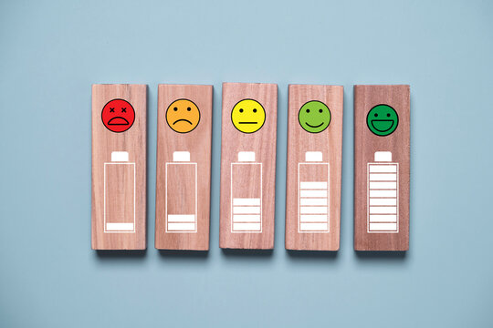 Wooden blocks showing battery levels and customer satisfaction icon from negative to positive for employee engagement, customer experience, wellbeing, performance improvement, and satisfaction rating.