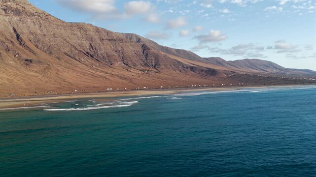 Cinematic Aerial Fly Over Famara Cliffs and Surfing Beach Coastline in Northwest Lanzarote at sunset