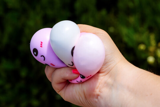 A hand holds three colorful dumpling shaped squishy toys in purple white and pink with smiling kawaii faces and blush marks against a green backdrop