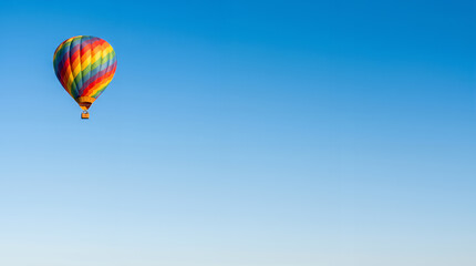 Fototapeta premium Vibrant rainbow-colored hot air balloon floating in a vast clear blue sky
