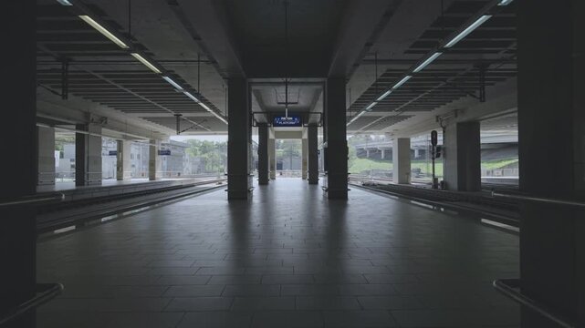 Symmetry view of empty train station platform with concrete pillars and digital signage during daylight.