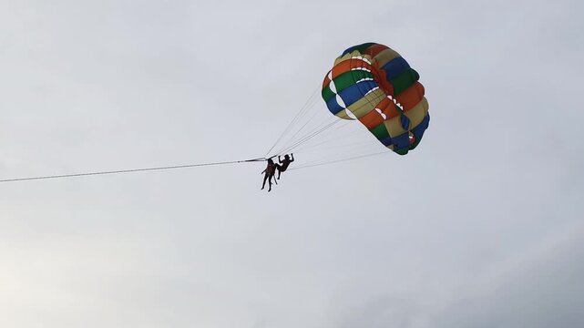 Peaceful sunset beach activities bring atmosphere to coastal resort. Enjoying sunset beach activities allows brave tourists to try colorful parasailing flight in warm evening sky.