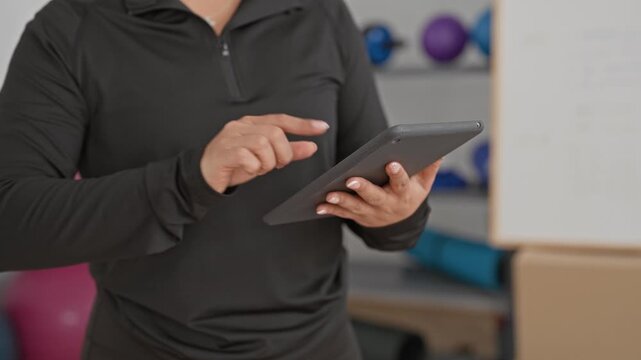 Woman tapping tablet with fingers in yoga training studio near exercise balls and whiteboard; training planning concentration.