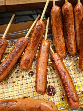 A collection of grilled or fried long hot dog sausages skewered on wooden sticks, placed on a wire rack