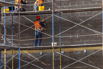 Naklejka premium Builders, standing on metal scaffolding, install a reinforcing mesh for applying plaster. The work at height is carried out by builders. Cladding works during the construction of the building.