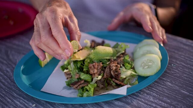 Closeup of a senior woman happily squeezing lime on fish and shrimp tacos at a taco stand in Baja California, Mexico.