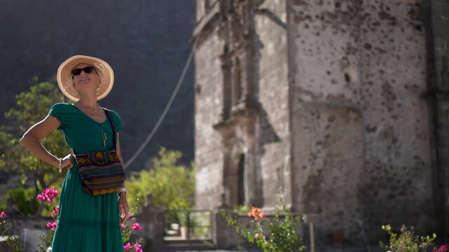 Mature woman strolls through the sunlit garden of San Javier Mission in Baja California Sur, enjoying the morning air and bright flowers