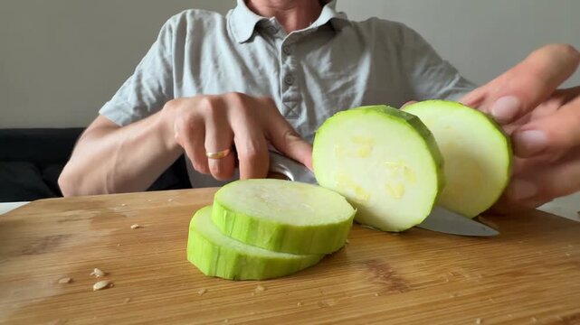 Cutting zucchini slices with kitchen knife on wooden board, fresh ingredients, healthy cooking, home kitchen