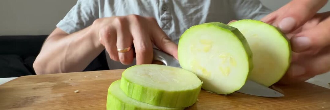 Slicing fresh zucchini into rounds on wooden cutting board, healthy vegetables, meal preparation, home cooking
