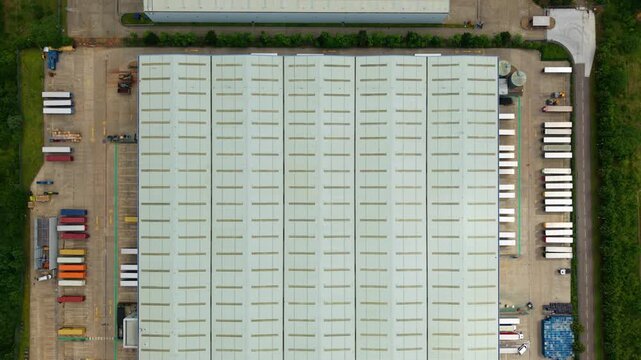 Top down aerial view of a large commercial distribution centre warehouse with rows of HGV lorries parked in loading bays.