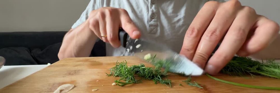 Chopping fresh dill herbs with chef knife on cutting board, cooking ingredients, home kitchen preparation