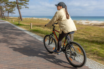 Fototapeta premium Woman cycling beside the sea. Active outdoor recreation on coastal path.