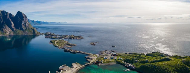 Aerial view of Lofoten near Reine and Reinebringen ridge, steep peaks left, small islands and bridges, turquoise coves, fishing village, causeway, calm water, Arctic light. © Aerial Film Studio
