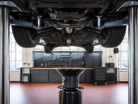 Vehicle underside on a lift during an oil change, with motor oil draining into a pan in a bright auto service workshop.