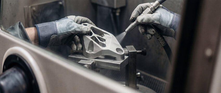 Gloved technician sandblasting 3d printed metal part in industrial manufacturing workshop for surface preparation