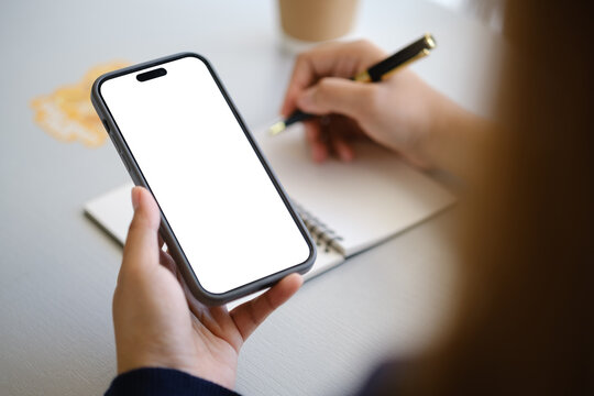 Mobile phone mockup with empty display beside a hand writing with a pen, for online planning, digital work, and UI design themes.