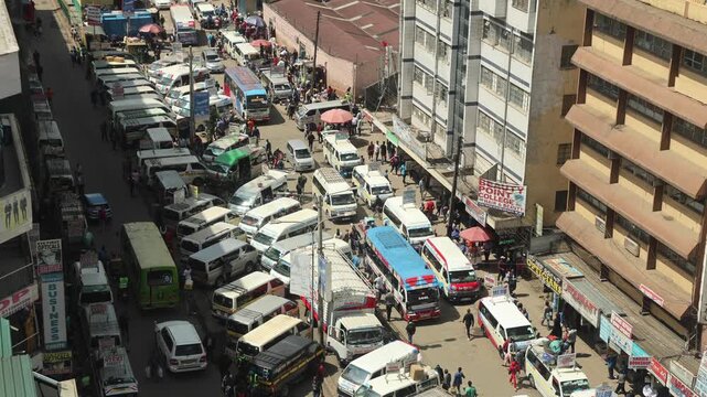 Nairobi, Kenya - 05 December 2024: View of congested city traffic with numerous matatu minibuses and buses parked along a narrow street lined with commercial buildings and pedestrians.