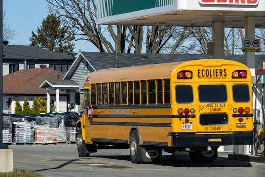 Quebec, Canada, 24 April 2026 : A yellow school bus stands at an Esso gas station with residential houses in the background.