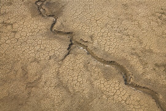 An aerial view of a dry riverbed with intricate crack patterns.