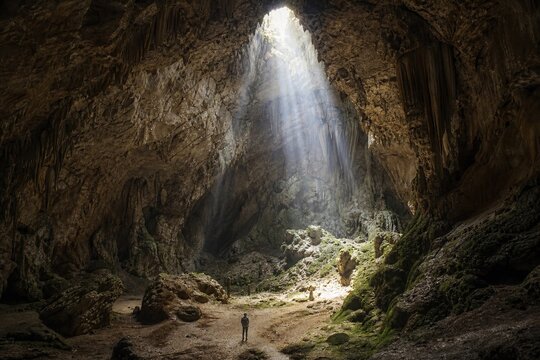 Vast interior of a towering limestone cave with light streaming down from a high ceiling opening.