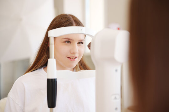 Happy teenage girl undergoing vision check with autorefractor