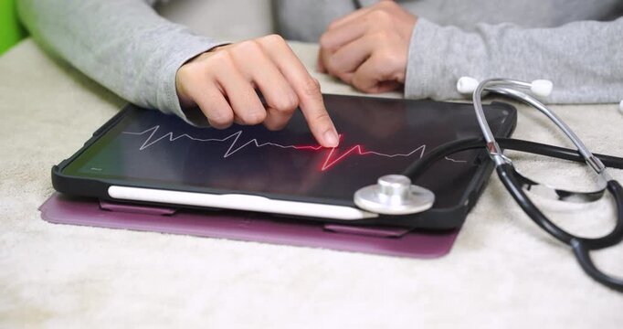 Close-up of a person touching an ECG waveform on a digital tablet beside a stethoscope during self health monitoring. Heart health, digital healthcare, preventive care, and medical technology concept.