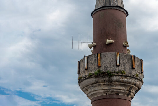 Mosque tower with loudspeakers and antenna under cloudy sky in an urban setting
