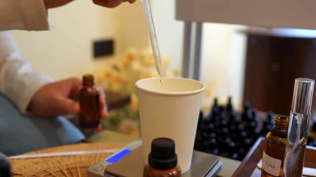 Close-up of using a pipette to measure essential oil into a mixing cup while creating handmade perfume. Fragrance formulation, perfume making, aroma blending, DIY cosmetics, and artisan workshop conce