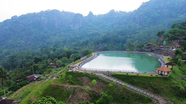 Aerial drone footage of Embung Nglanggeran, a scenic artificial reservoir located in the Ancient Nglanggeran Volcano area, Yogyakarta, Indonesia.