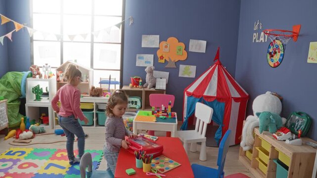 Girl reaches to toss a blue ball by red circus tent and table of blocks in a colorful indoor playroom inside building; joyful playtime.