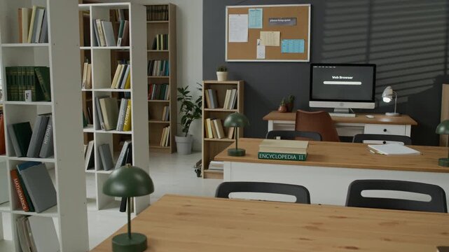 Empty modern library study room featuring wooden desks, bookshelves, and computer monitor panning slowly. Clip is perfect for educational marketing, online learning promos, or school advertisements