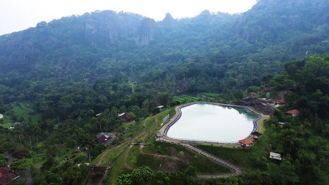 Aerial drone footage of Embung Nglanggeran, a scenic artificial reservoir located in the Ancient Nglanggeran Volcano area, Yogyakarta, Indonesia.
