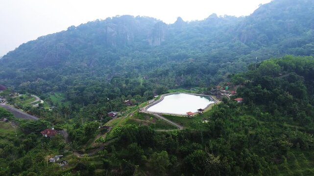 Aerial drone footage of Embung Nglanggeran, a scenic artificial reservoir located in the Ancient Nglanggeran Volcano area, Yogyakarta, Indonesia.