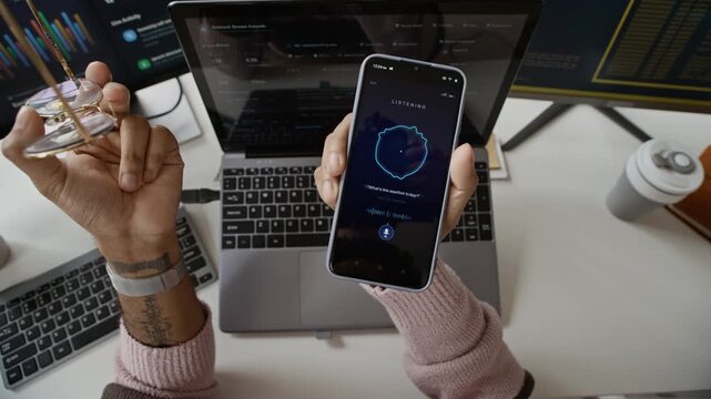 POV cropped shot of hands of developer testing voice assistant app on smartphone at office desk with laptop. Video is ideal for commercial advertisements of smart assistant software