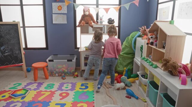 Girl reaching into a toy kitchen cabinet with toys scattered on a number mat in a playroom inside a building; playful curiosity.