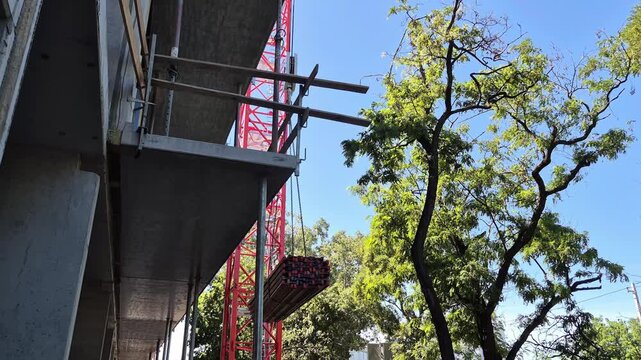 Slow motion video capturing a tower crane precisely lowering a bundle of wooden I-joists next to the structure of a house.