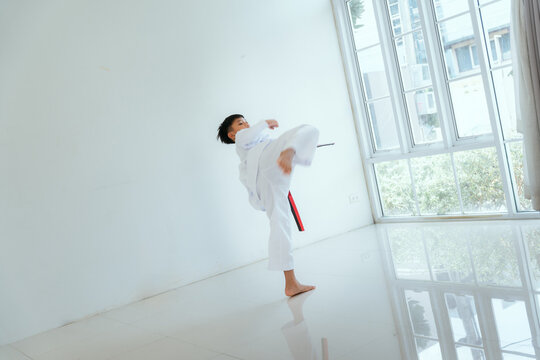 Child practices martial arts kick indoors with focus and determination during training session in bright room