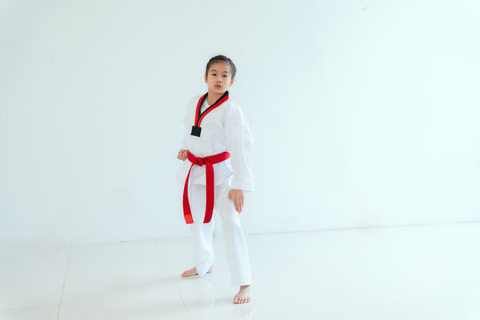 Young girl practices martial arts in a white uniform with a red belt in a bright room