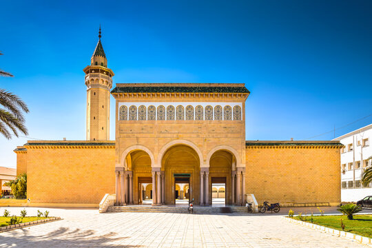 Frontal view of the famous Habib Bourguiba Mosque entrance with three traditional arches and a minaret tower under a blue sky in Monastir, Tunisia.