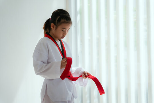 Young girl ties red belt in martial arts uniform in a white room during training session