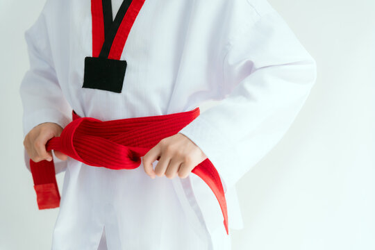 Young girl ties red belt in martial arts uniform in a white room during training session