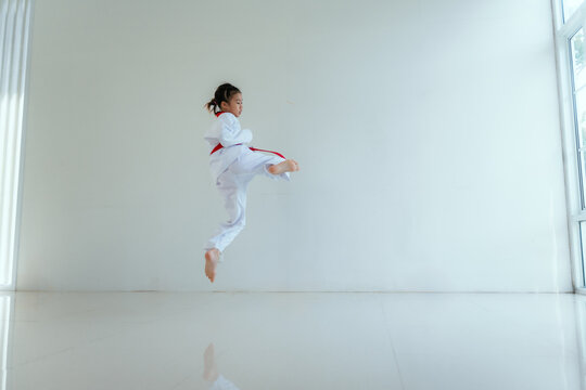 Child practices martial arts with a jump kick in a bright indoor space during training session