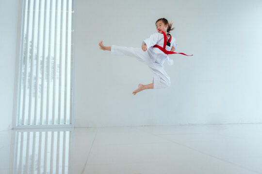 Child practices martial arts with a jump kick in a bright indoor space during training session