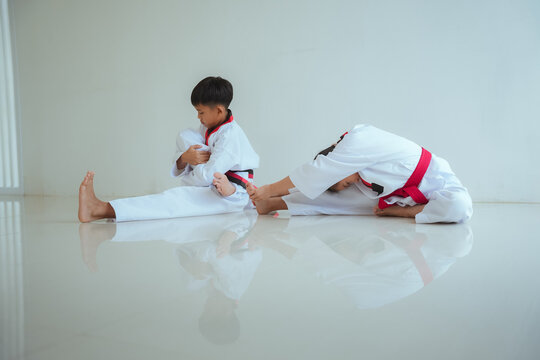 Young children practice stretching exercises in a bright room during a martial arts class in the afternoon